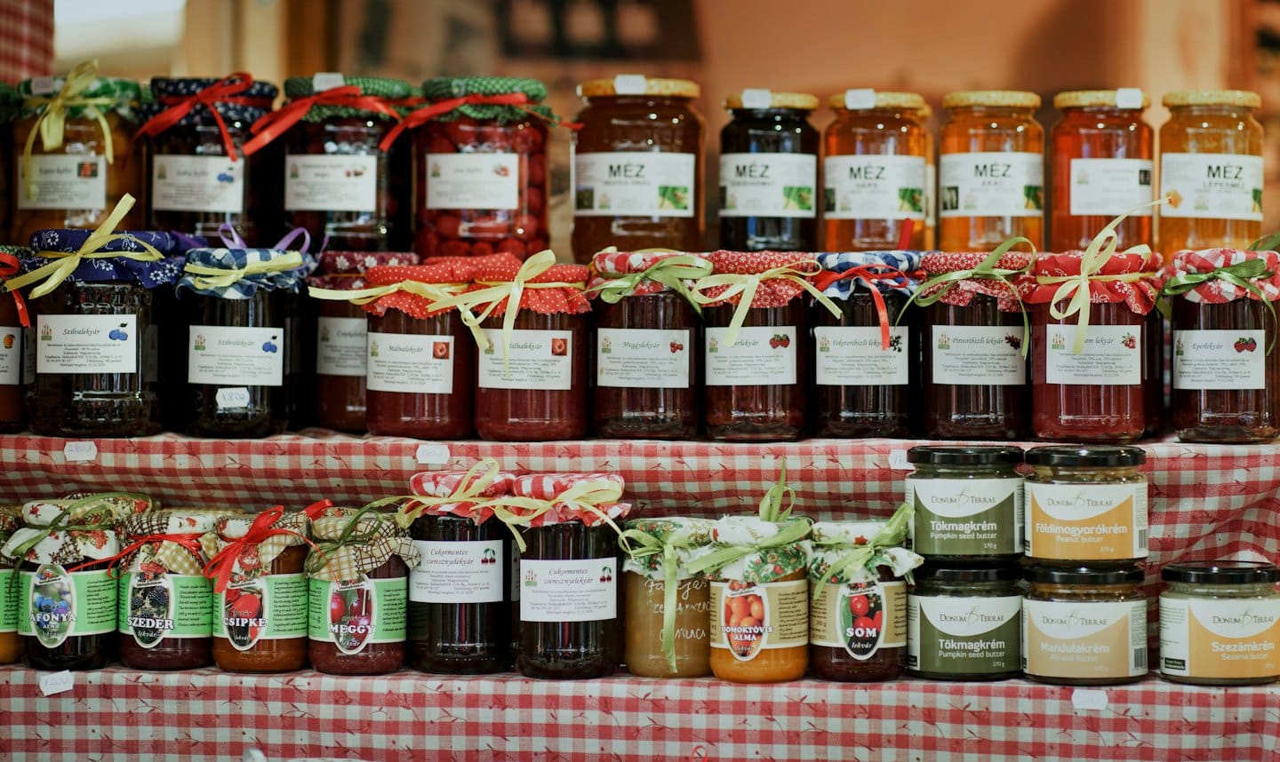 Boccali artigianali di miele, marmellate e creme di frutta secca su una tovaglia a scacchi.